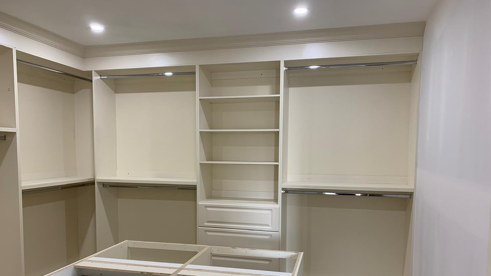 Walk-in closet with white shelving, a drawer bank and hanging sections — one of the company's own closets