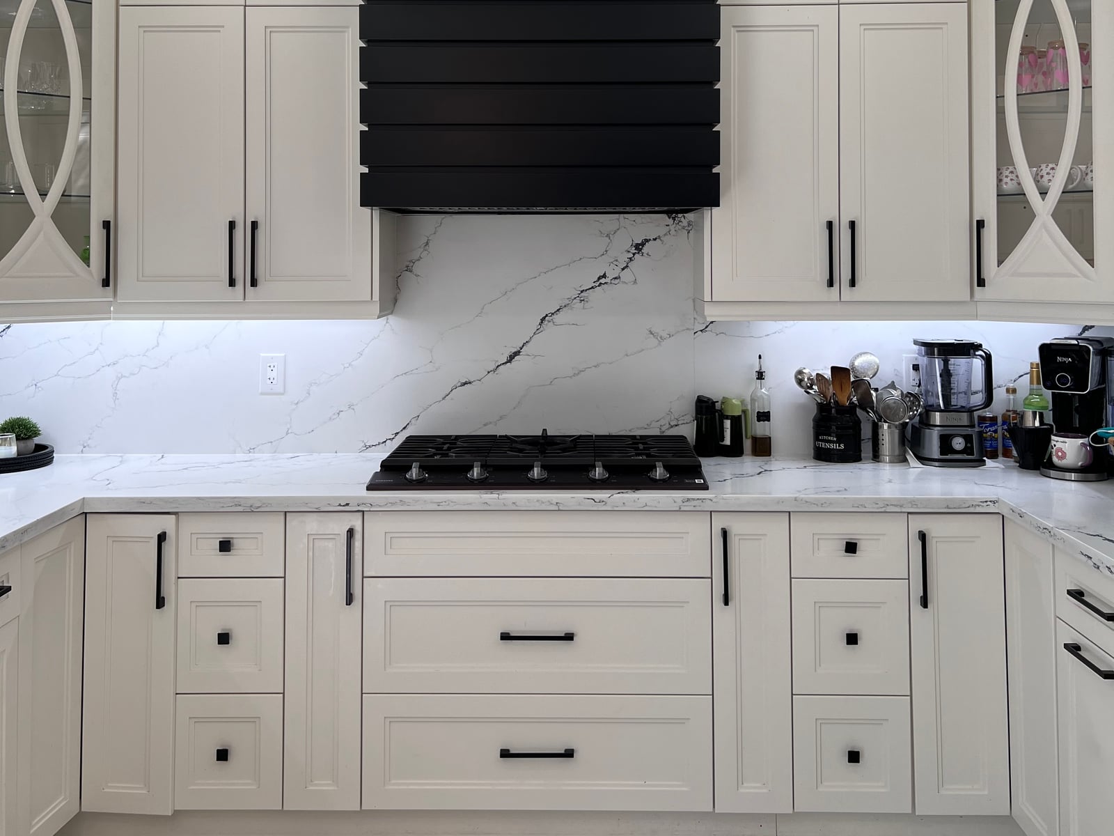 Kitchen with white cabinetry, glass-front display cabinets, a black decorative hood surround and veined countertop and backsplash surfaces — October 2026 catalogue