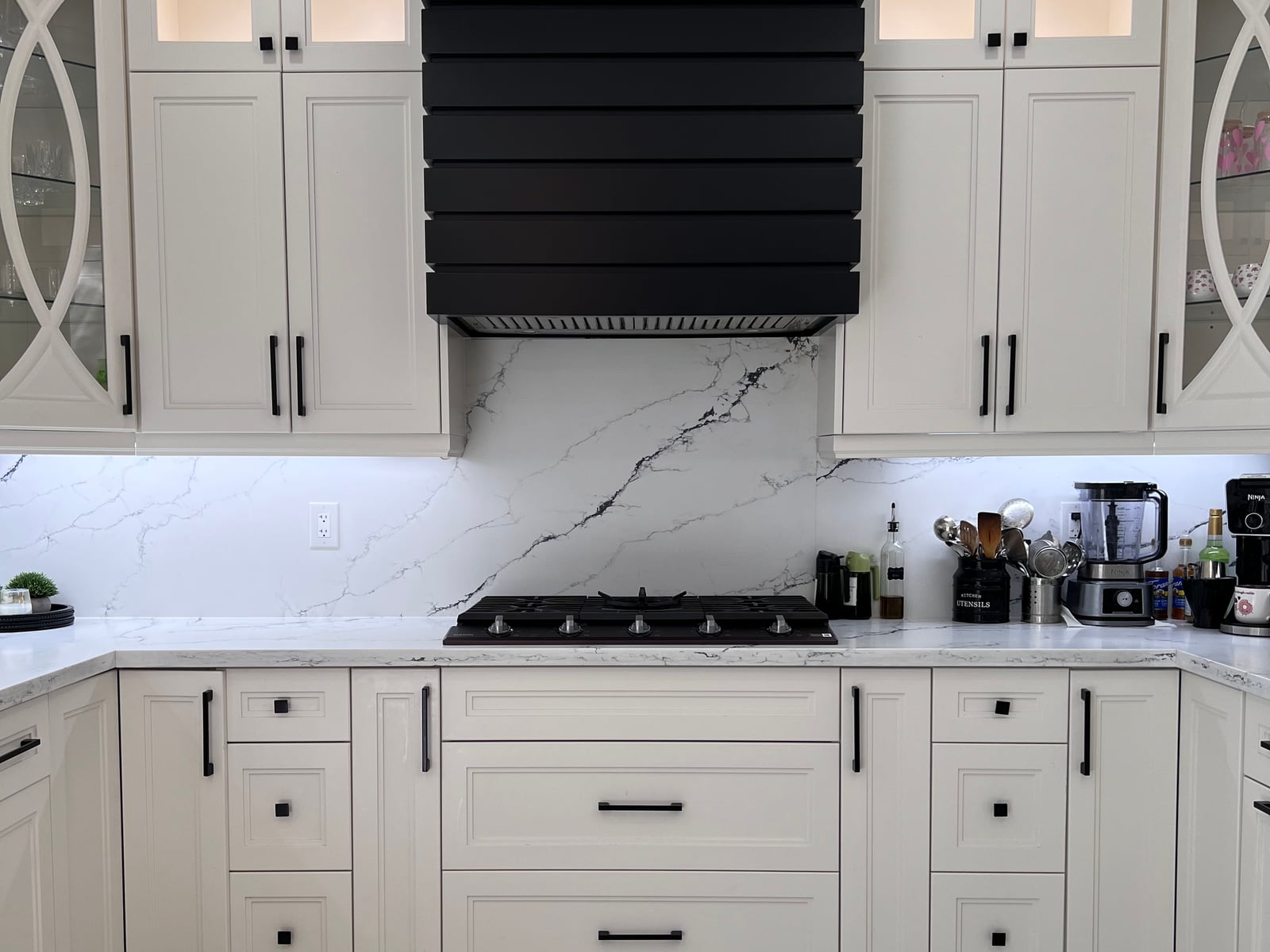Cooktop under a decorative hood surround with backsplash and large-format tile flooring — a kitchen from the October 2026 catalogue