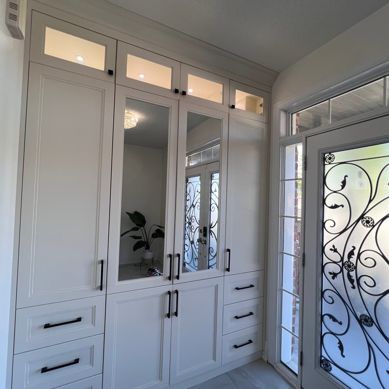 Entry-area built-in cabinetry with mirrored doors, drawers and lit upper display compartments
