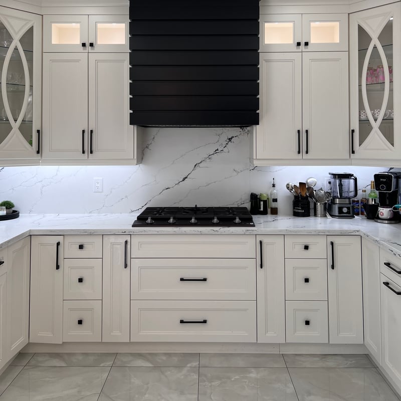 Kitchen with white cabinetry, glass-front display cabinets, a black decorative hood surround and veined quartz countertop and backsplash