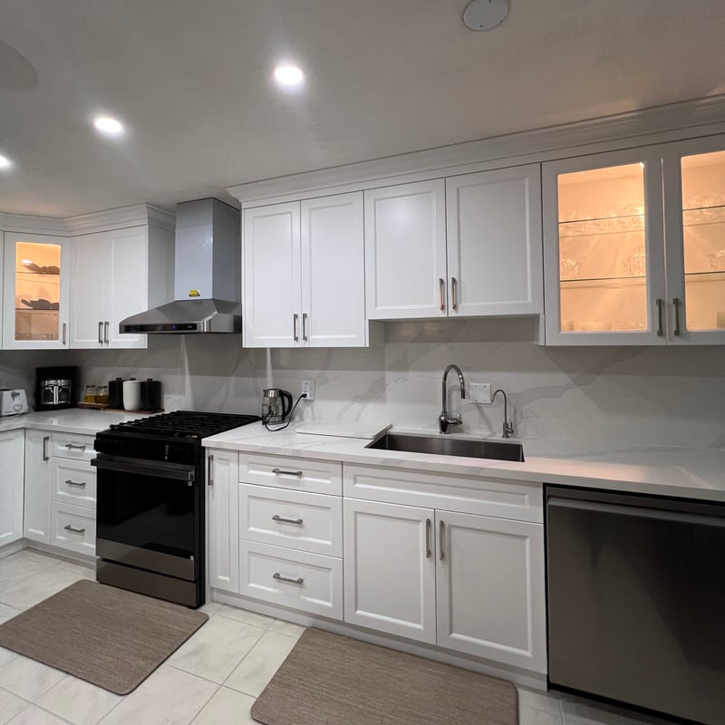 White kitchen cabinetry with illuminated glass-front upper doors, stainless hood and a marble-look backsplash