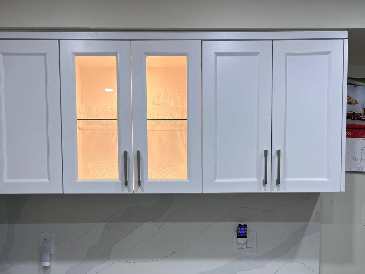 Illuminated glass-front upper cabinets over a marble-look backsplash