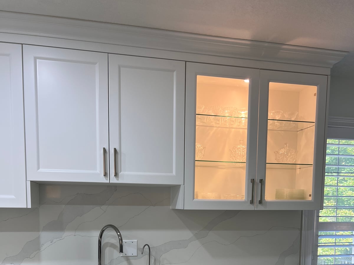 Sink wall under a window with glass-front upper cabinets and a marble-look backsplash