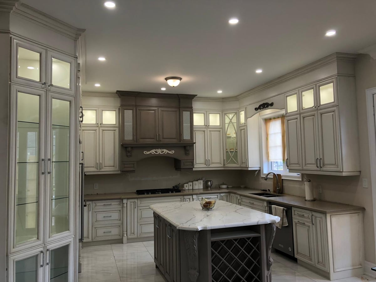 Traditional kitchen in a grey glazed finish with raised-panel doors, a carved hood and a large island with seating