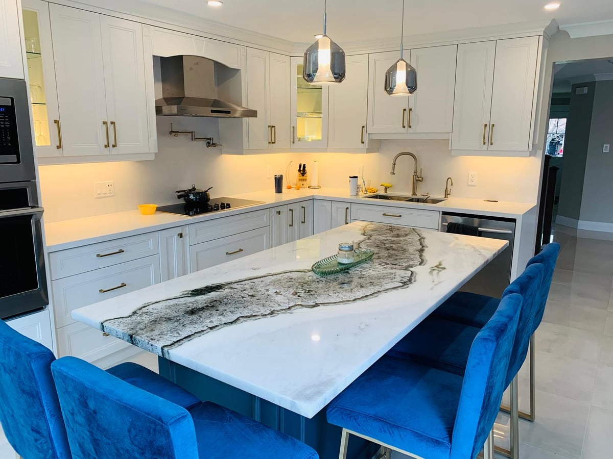 White kitchen with a dramatically veined island top, pendant lights and blue chairs