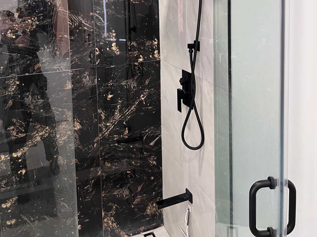 Shower with black marble-look porcelain walls, matte black fixtures, a rain head and a glass panel