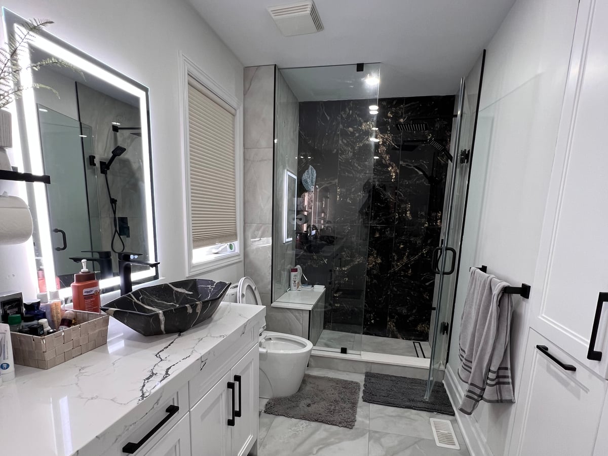 Bathroom with a double vanity, lit mirrors and a glass shower enclosure