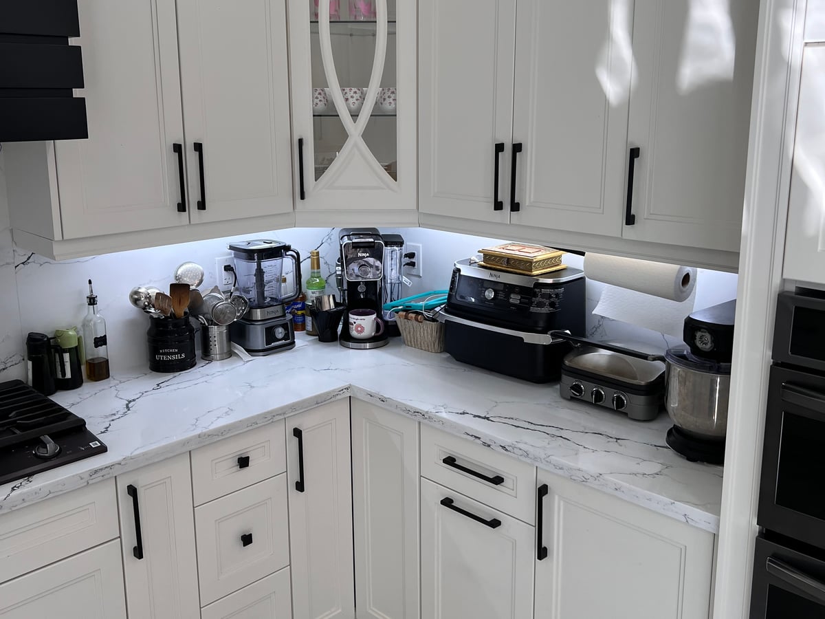 Gas cooktop under the black hood surround, white cabinets and drawers below, veined quartz backsplash